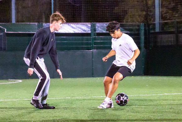 two teenage boys playing football on artificial pitch